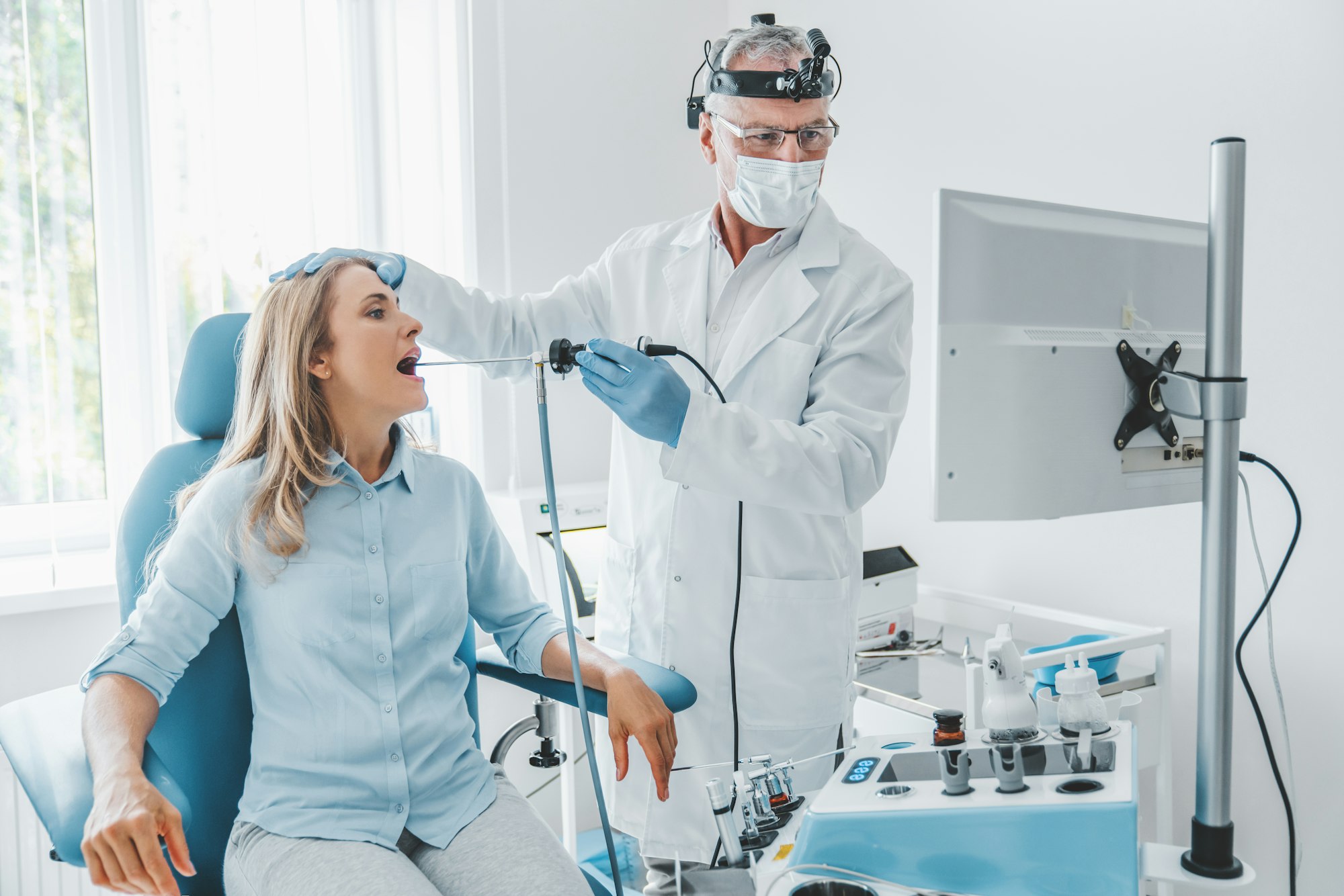 Senior otolaryngologist making endoscopic examination while looking in monitor for female